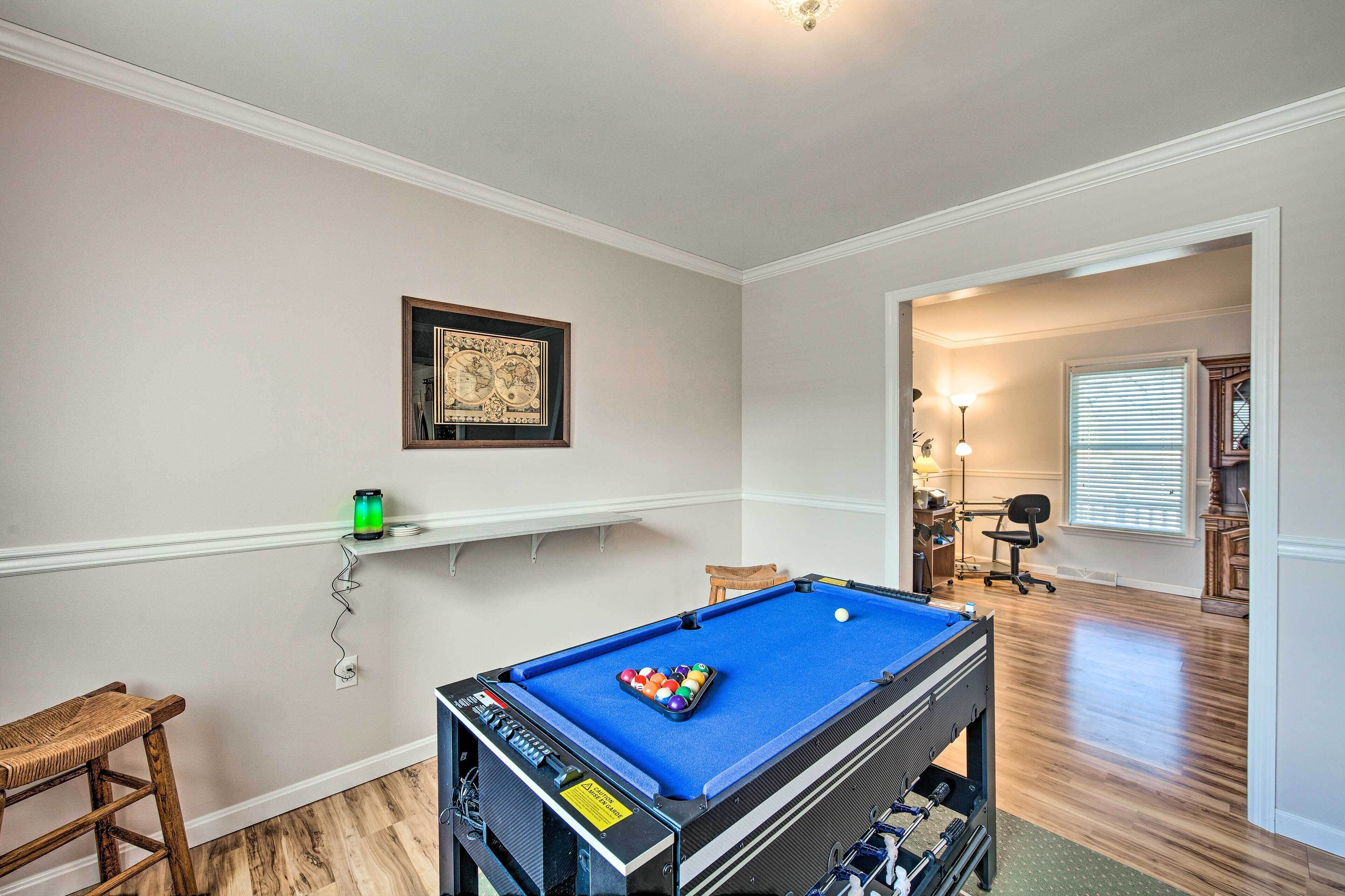 A pool table in a room with a wooden floor, a framed picture on the wall, and a chair.