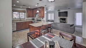 A modern kitchen with granite countertops, wooden cabinets, and a central island. There is a dining area with a table and chairs, and a fireplace in the living room. - Parker Home on the Colorado River w/ Views! (Parker)