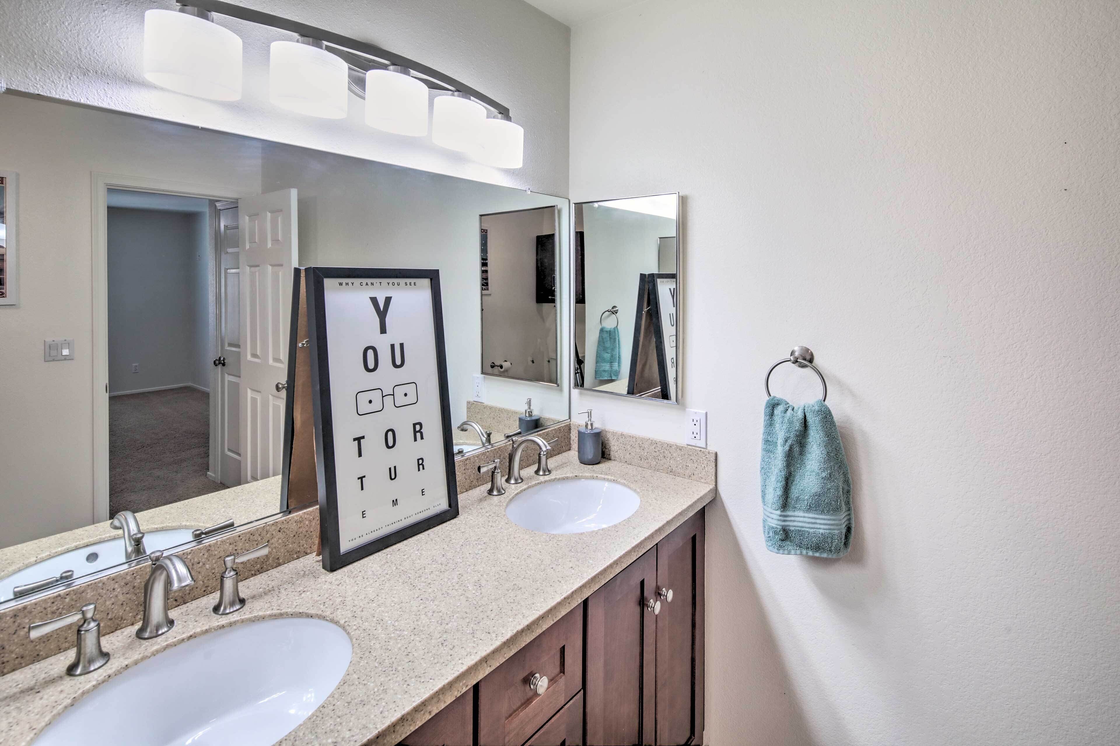 A bathroom with two sinks, a large mirror, and a framed sign.