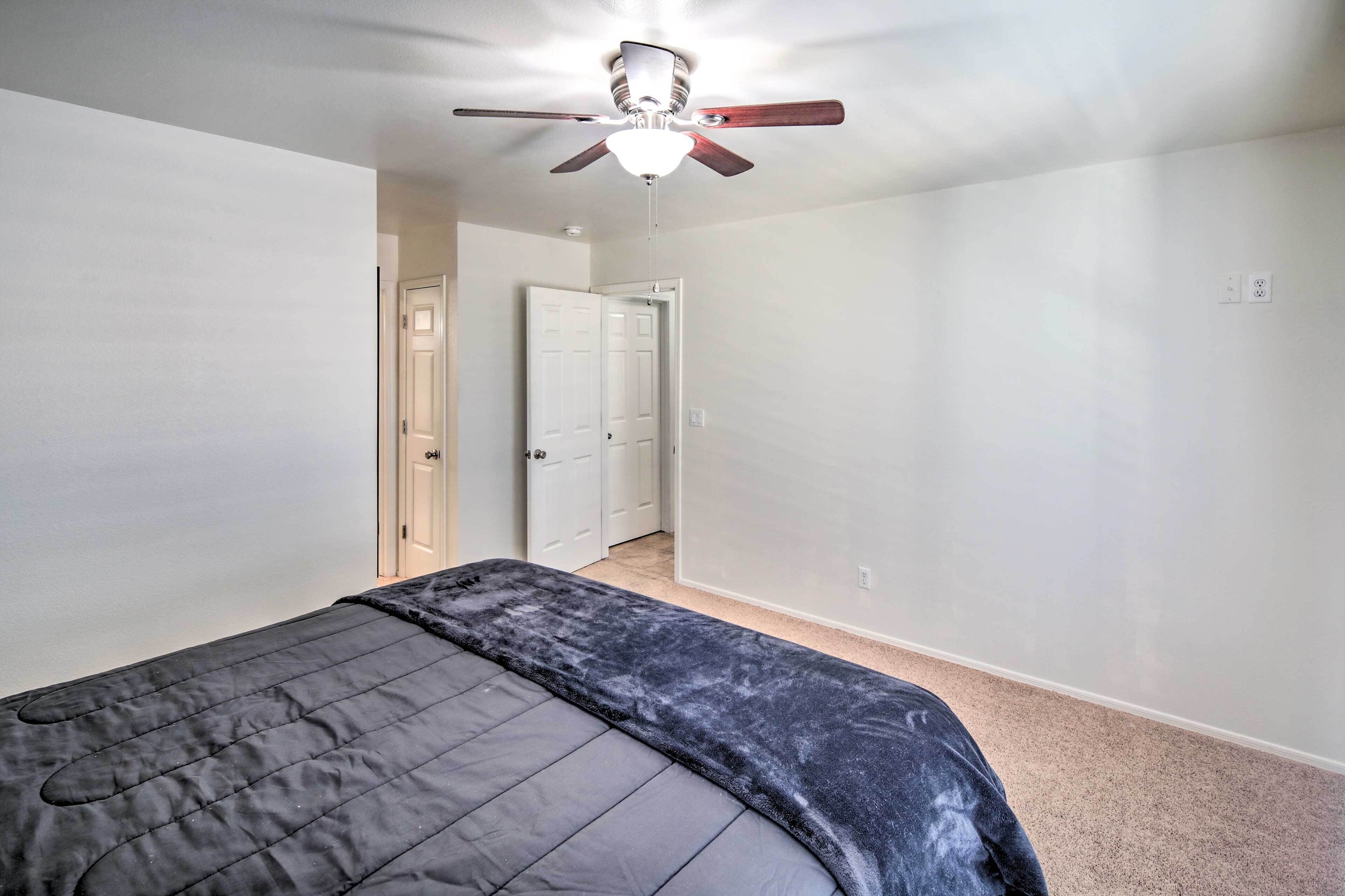 A bedroom with a bed, a ceiling fan, and a door leading to another room.