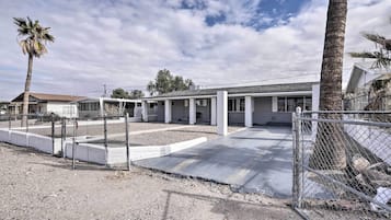Una propiedad residencial con patio cercado, terraza techada y edificio de una sola planta con techo plano.