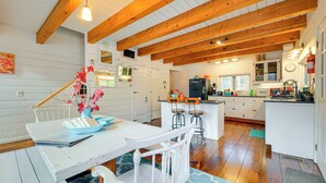 A kitchen with wooden beams, white cabinets, a dining area with a table and chairs, and a refrigerator.