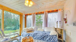 A cozy bedroom with a large bed, a wicker chair, a small table, and a window with curtains.