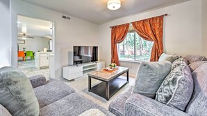 Un salon moderne avec des canapés gris, un téléviseur à écran plat, une table basse et une fenêtre ornée de rideaux orange.