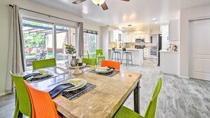 Un coin repas avec une table en verre, des chaises vertes et oranges, et un ventilateur de plafond.