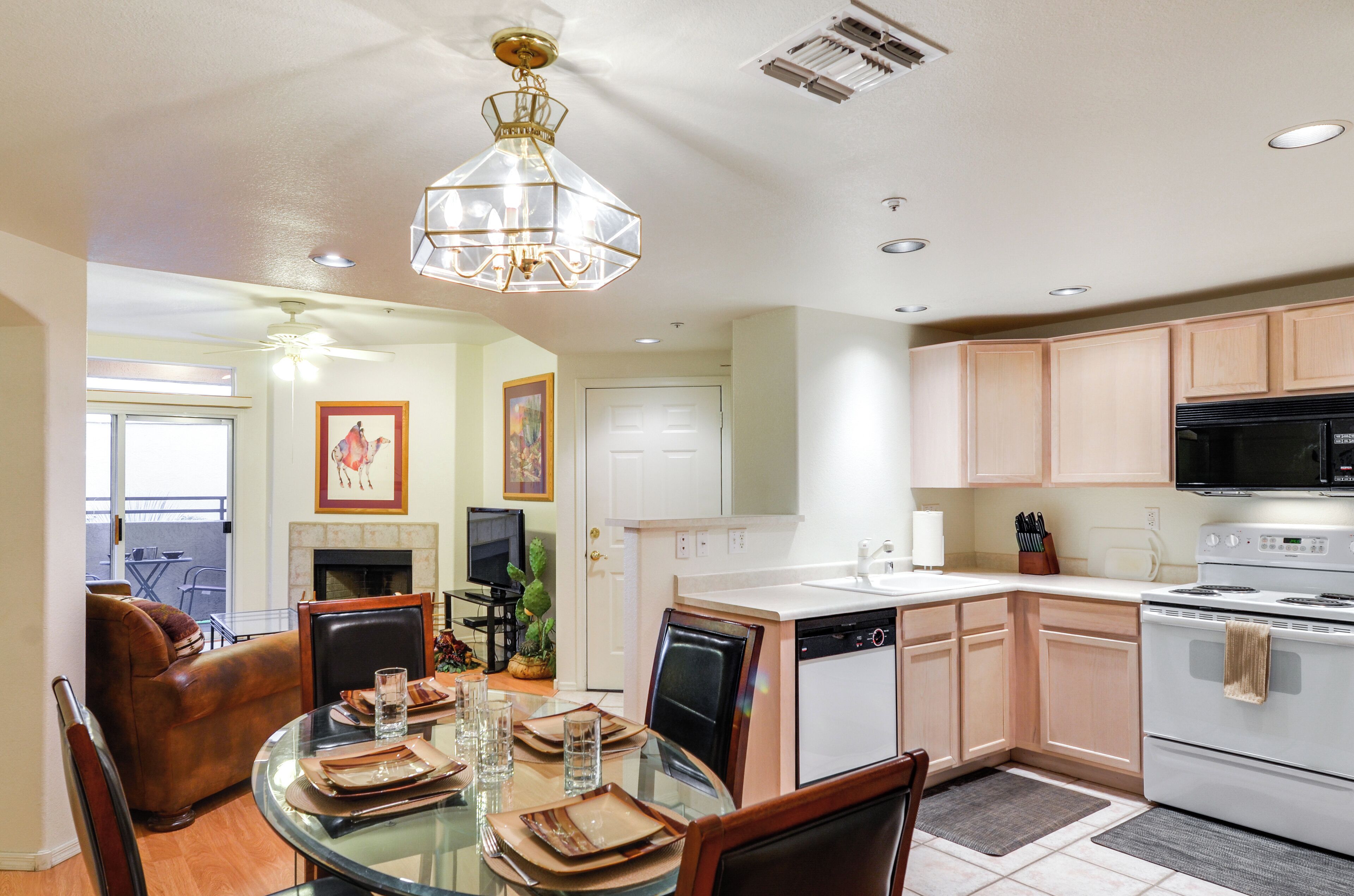 A modern kitchen with a dining area, featuring a glass table, wooden chairs, a built-in oven, and a microwave.