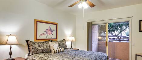 A bedroom with a bed, two bedside lamps, a ceiling fan, a framed picture on the wall, and a view of the outside through a sliding door.