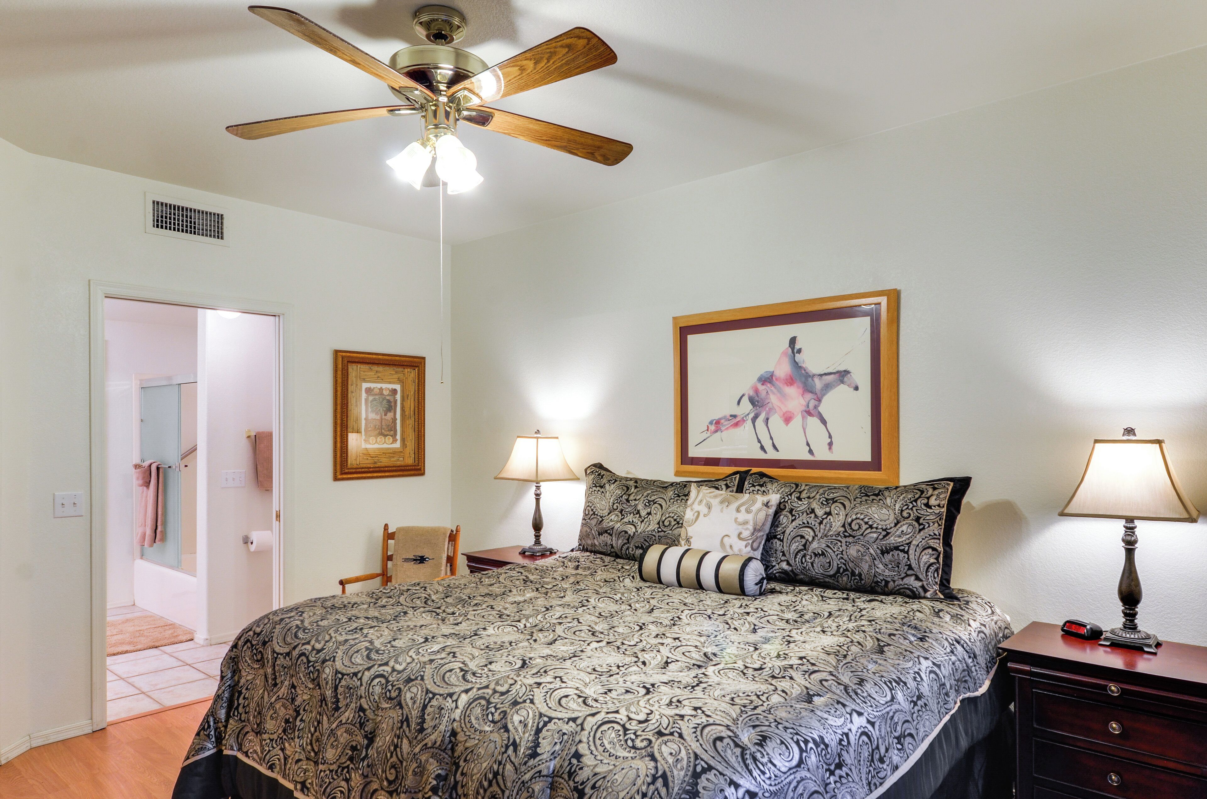A bedroom with a bed, two bedside tables, a ceiling fan, and a door leading to a bathroom.