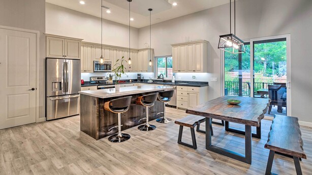 A modern kitchen with a central island, bar stools, a dining table, and a large window providing a view of the outdoors. - Sedona Retreat w/ Patio, Bar & Swim Spa! (Sedona)