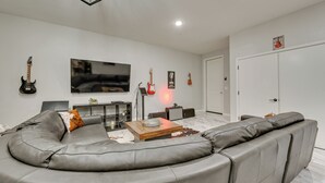 A modern living room with a curved grey sofa, a flat-screen TV, and guitars on the wall. - Sedona Retreat w/ Patio, Bar & Swim Spa! (Sedona)