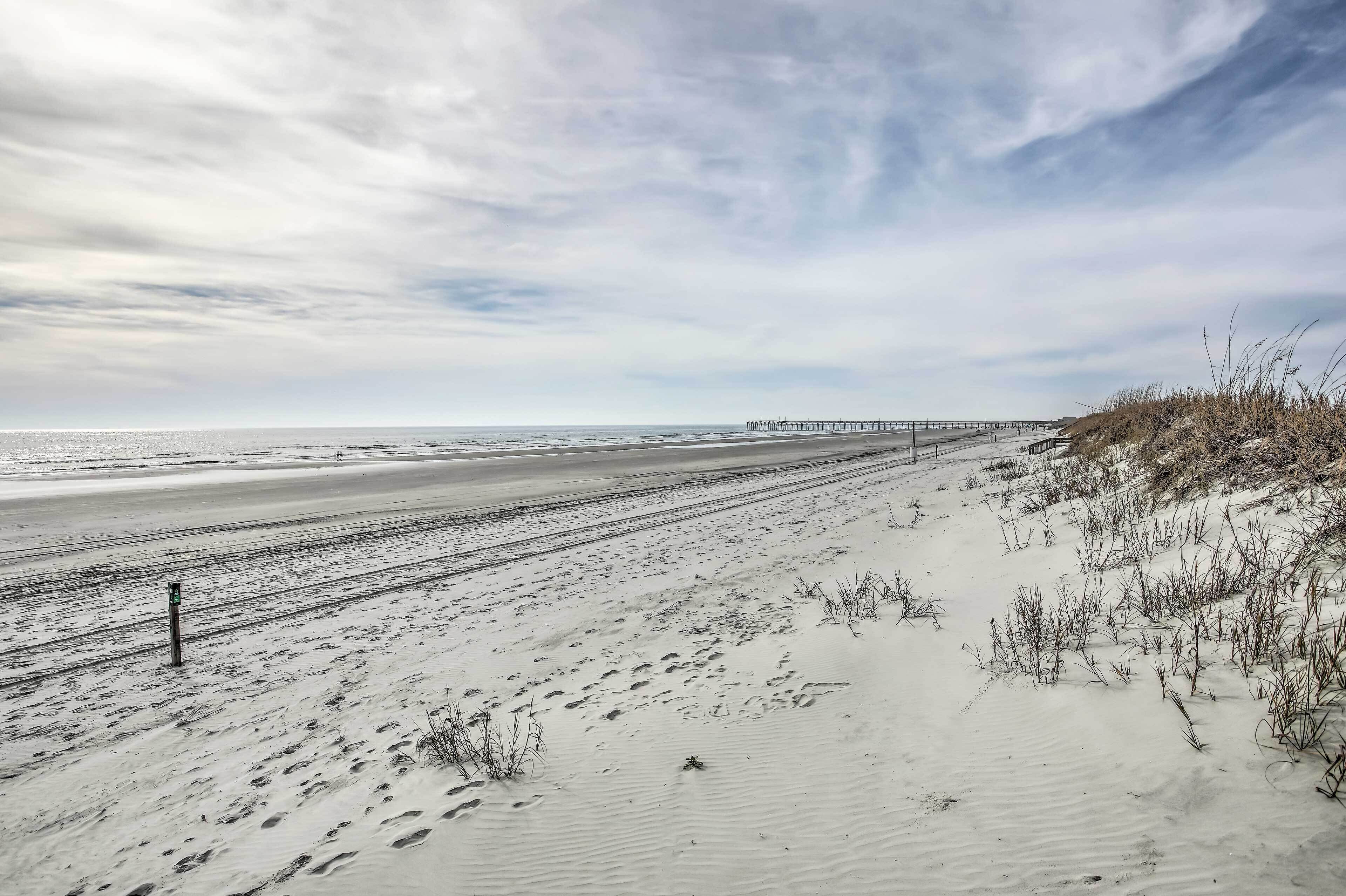 A beach with sand dunes and a pier in the distance.