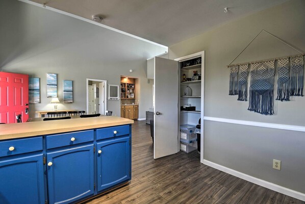 A kitchen with blue cabinets, a red door, and a wall-mounted macrame decoration. - Steps to Sunset Beach: Canal-front Home w/ Dock! (Sunset Beach)