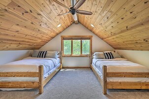 Un dormitorio con dos camas de madera, un ventilador de techo, una ventana y suelo alfombrado.