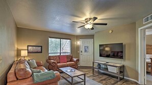 A living room with a brown leather couch, a coffee table, a ceiling fan, and a television on the wall. - Tucson Desert Retreat w/ Pool + Hot Tub Access! (Tucson)