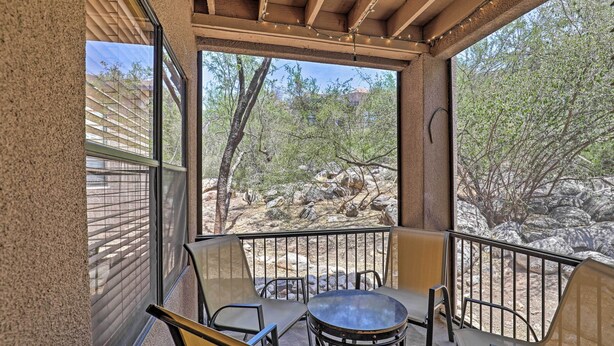 A covered outdoor seating area with a table and chairs, overlooking a rocky landscape with trees. - Tucson Desert Retreat w/ Pool + Hot Tub Access! (Tucson)