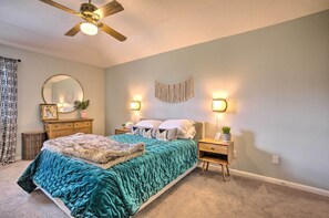 Un dormitorio con cama, mesitas de noche, cómoda, ventilador de techo, espejo y apliques de pared.