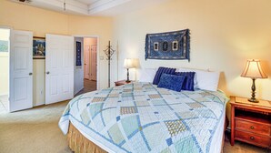 Un dormitorio con una cama grande, una mesita de noche con lámpara, una puerta que da a otra habitación y un cuadro colgado en la pared.
