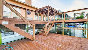 Una terraza de madera con una escalera que lleva a una zona cubierta, un barco amarrado en el agua y un letrero que solicita no arrojar agua.