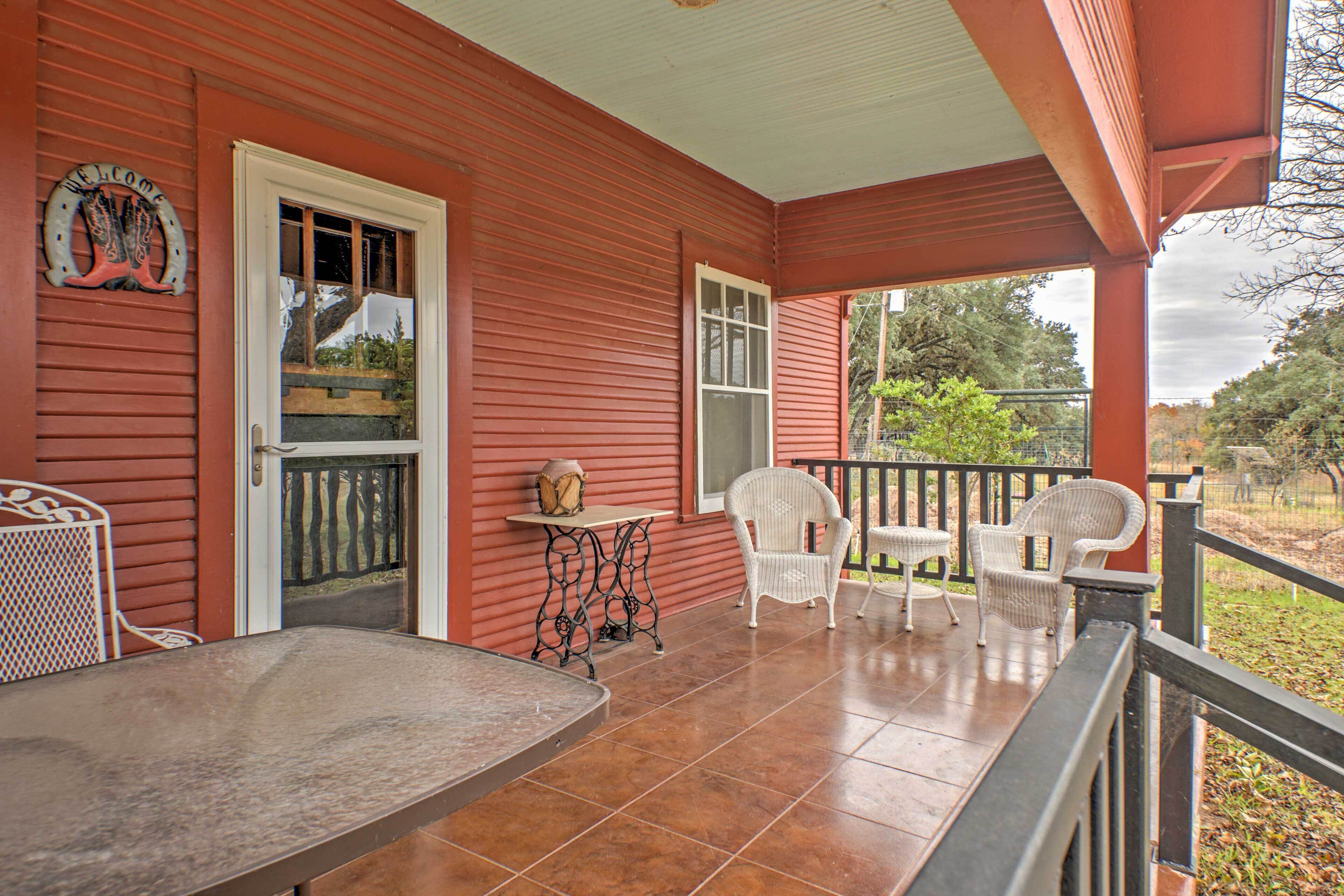 A red wooden porch with a white table and four wicker chairs.
