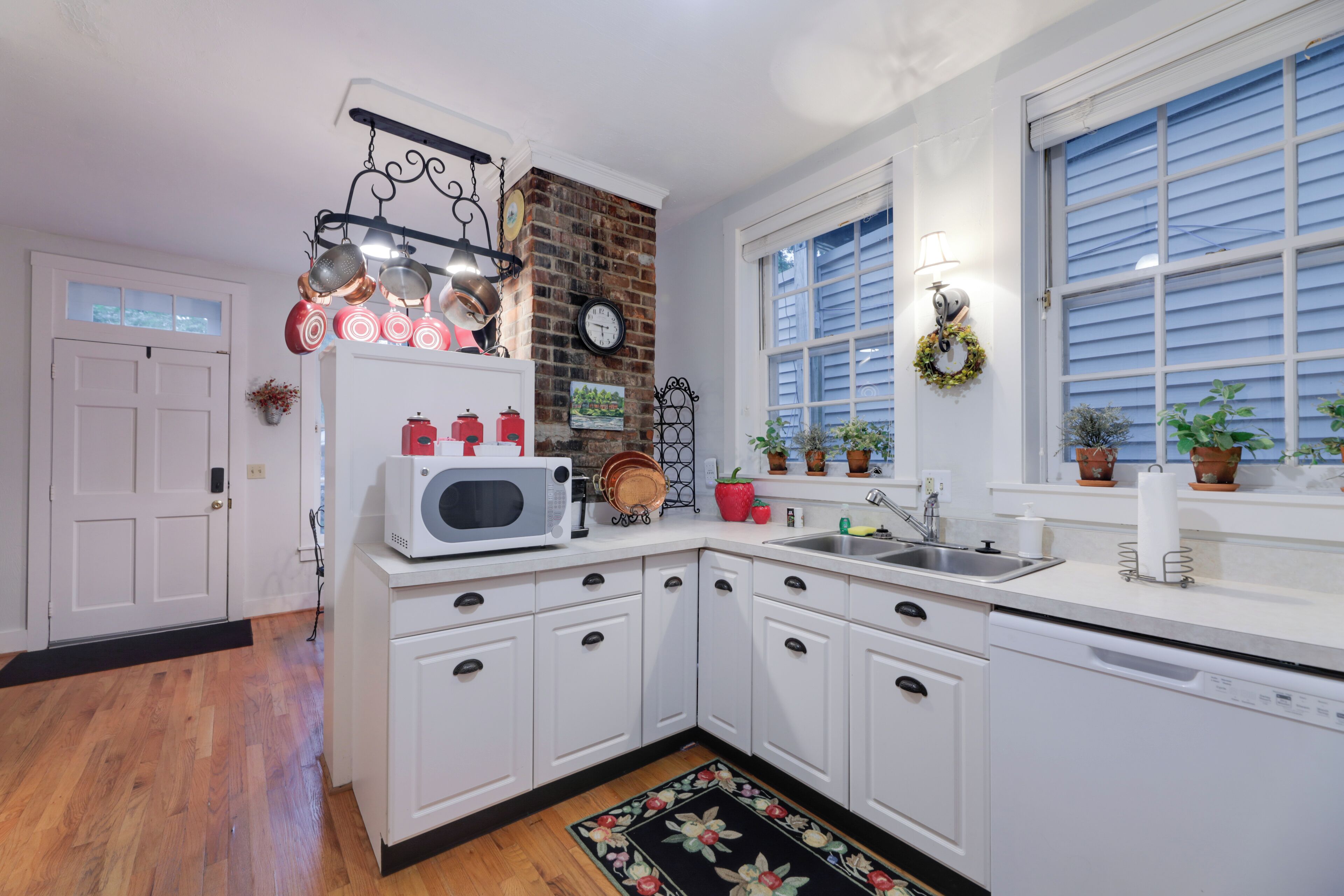 A kitchen with white cabinets, a microwave, a sink, and a window with blinds.
