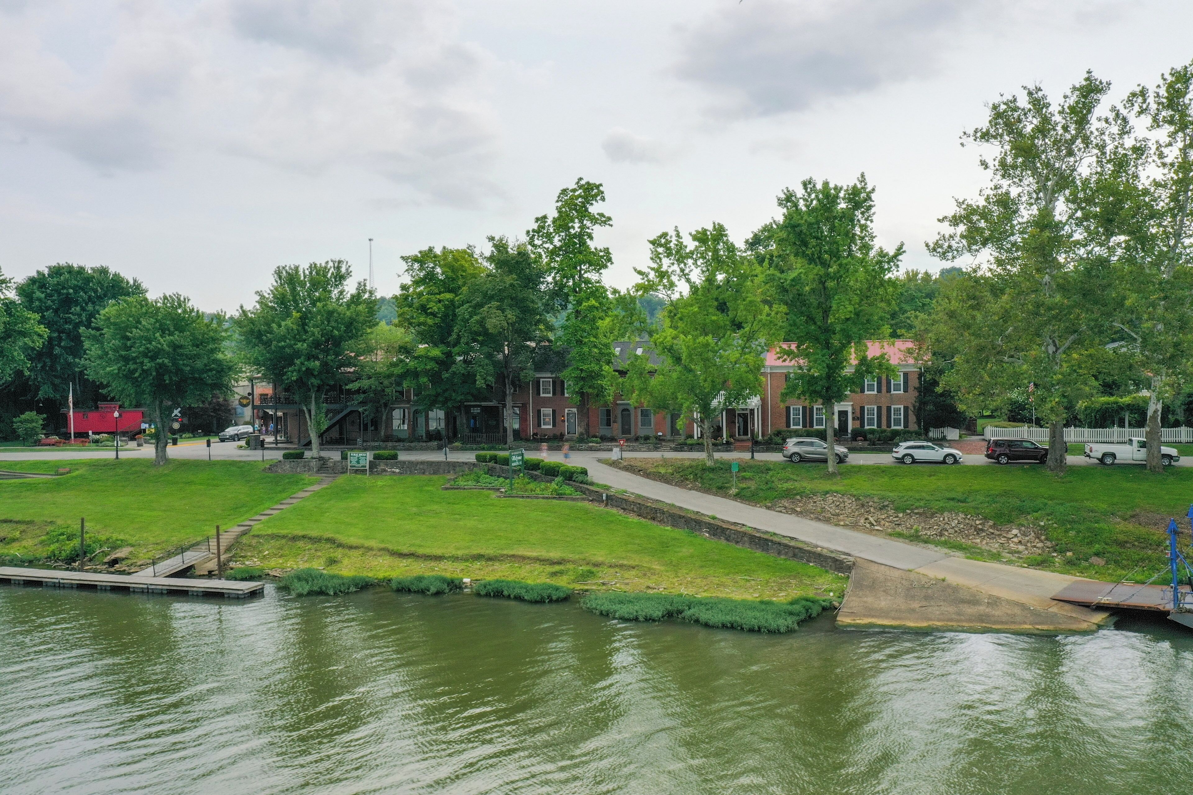 Un parque a orillas del río con un sendero, bancos y un muelle.