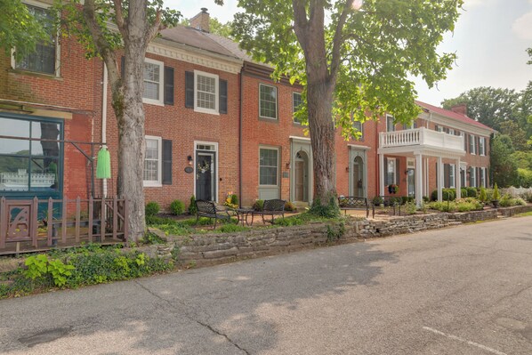 A row of brick buildings with a stone wall and benches in front. - Riverfront Studio w/ Private Patio & Garden! (Augusta)