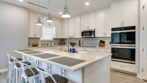 A modern kitchen with white cabinets, a large island with bar stools, stainless steel appliances, and pendant lighting. - Picturesque Texas Gulf Coast Home in Port Isabel! (Port Isabel)