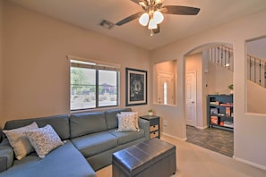 A living room with a grey sectional sofa, a ceiling fan, and a window with blinds.