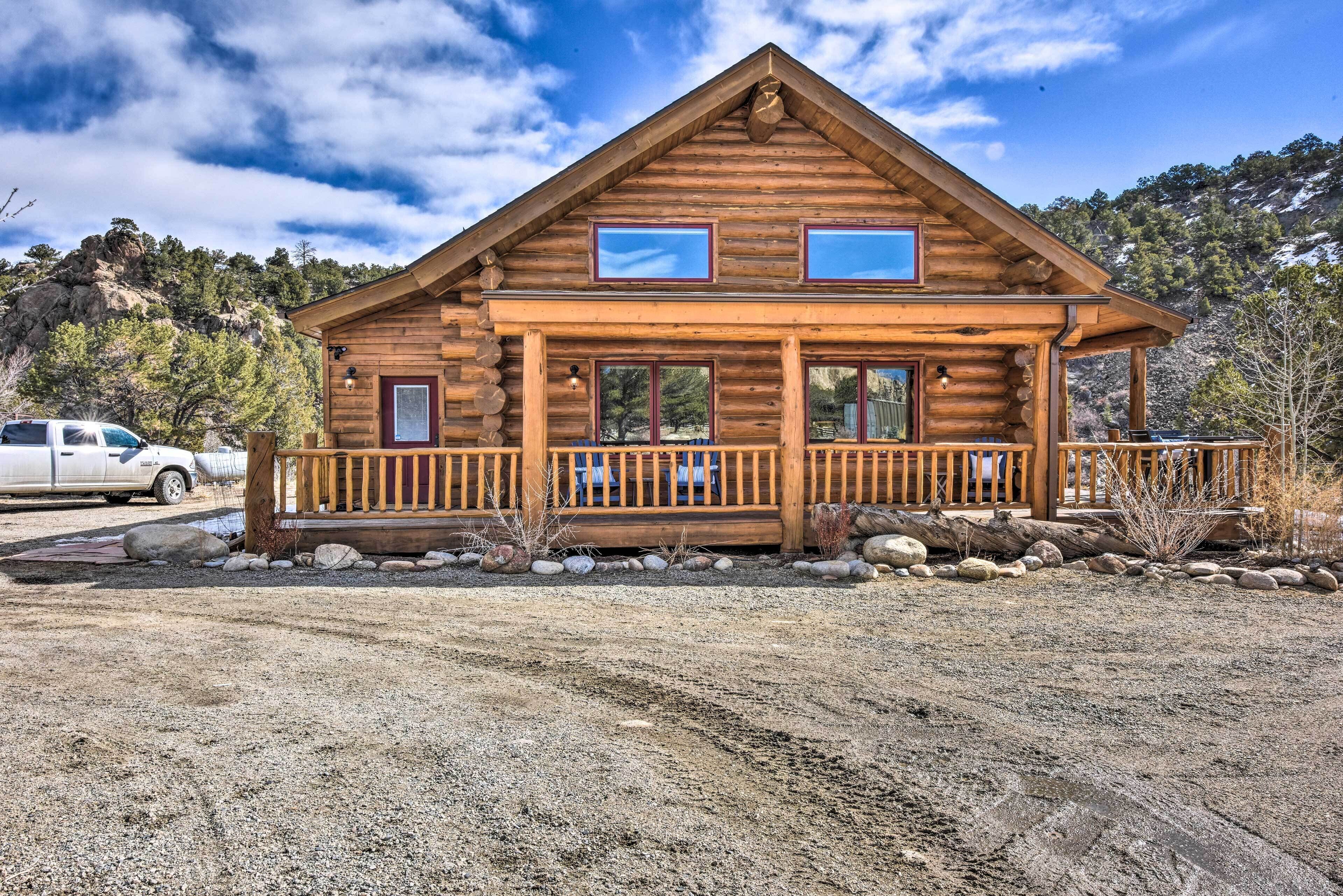 A log cabin with a porch, large windows, and a view of a mountainous landscape.