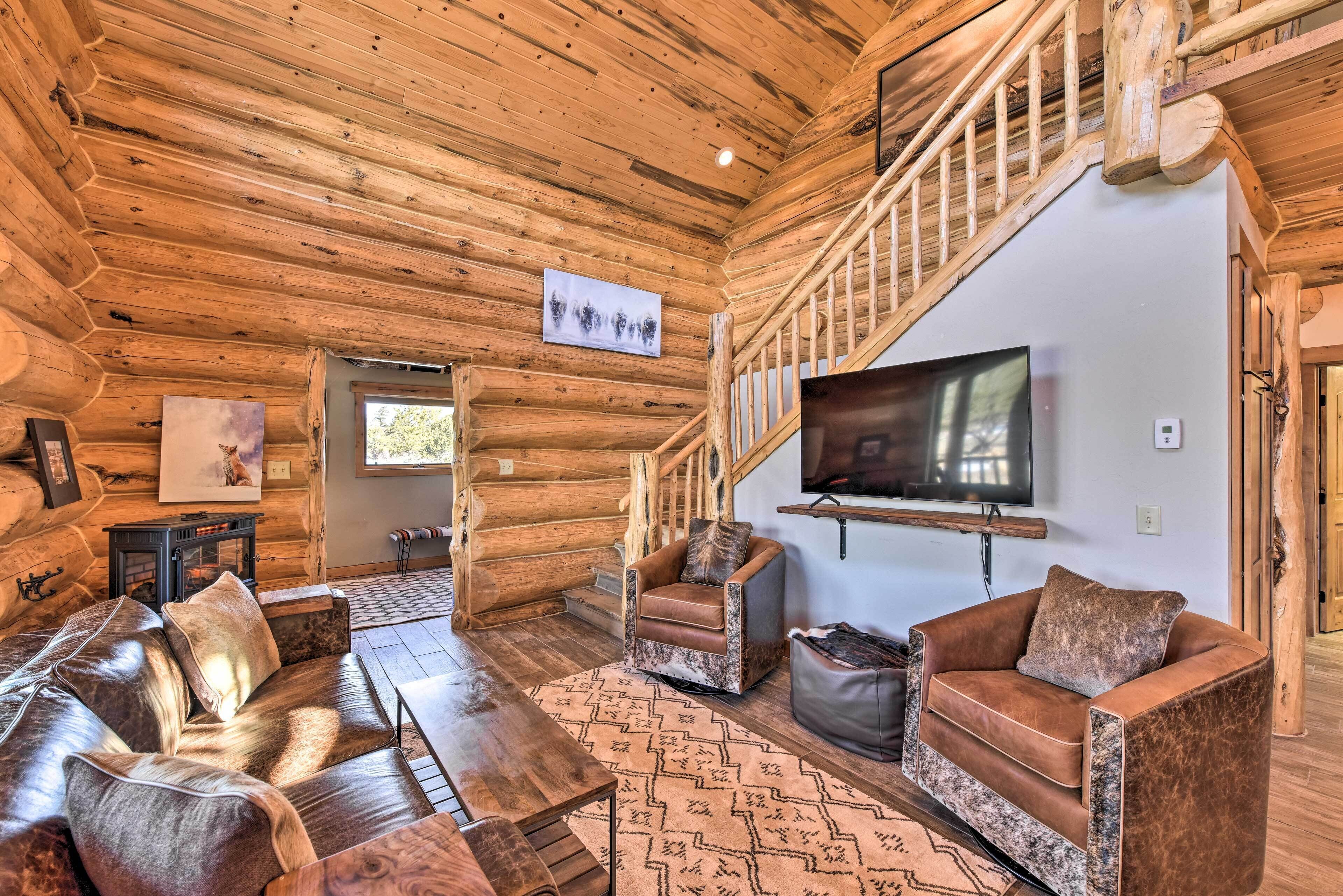 Ein rustikales Blockhaus-Interieur mit Kamin, Ledersofas, Fernseher und einer Treppe.
