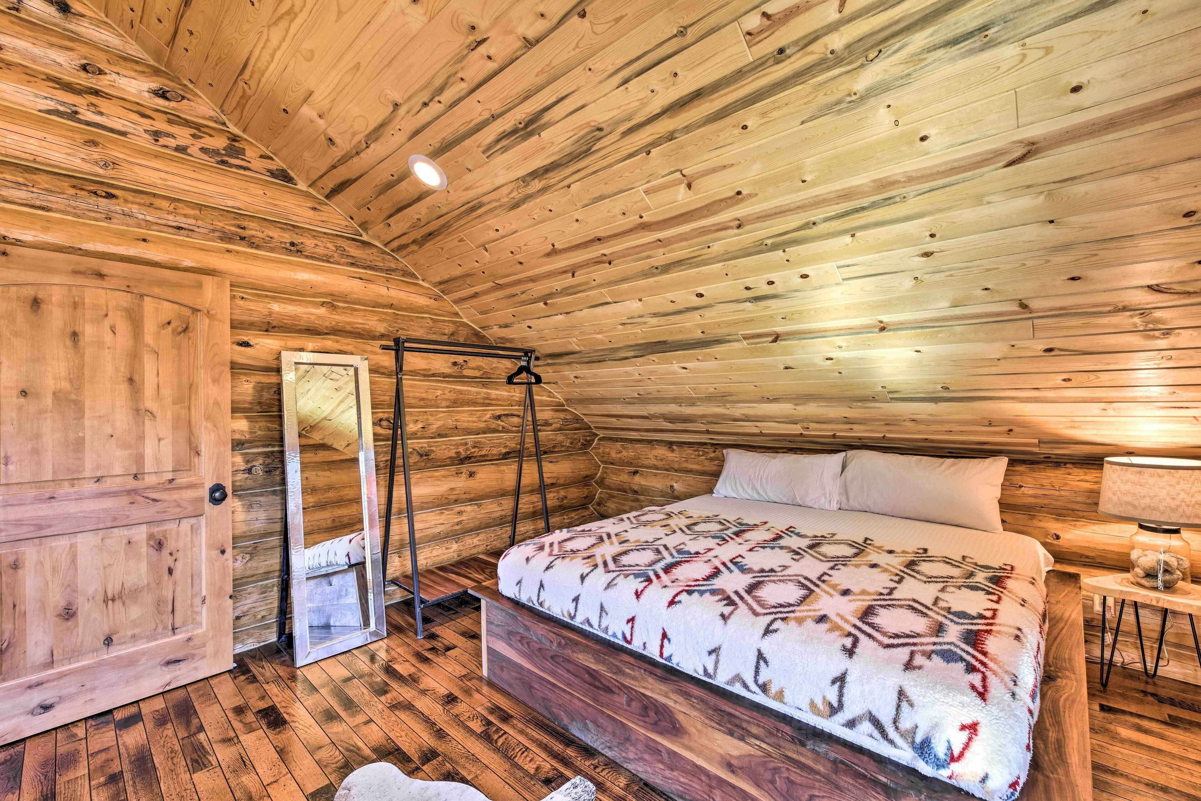 A wooden cabin bedroom with a bed, a hanging chair, and a wooden door.