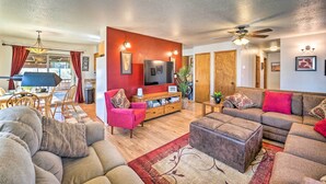 A spacious living room with a large sectional sofa, a red accent wall, a television, and a dining area with wooden furniture.