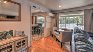 A modern living room with a leather sofa, dining area, and a large window offering a view of a lake. - 'the Grey Goose': Waterfront Home With Beach (New Bern)
