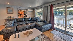 A modern living room with a leather sectional sofa, a white coffee table, and a view of a lake through large sliding glass doors. - 'the Grey Goose': Waterfront Home With Beach (New Bern)