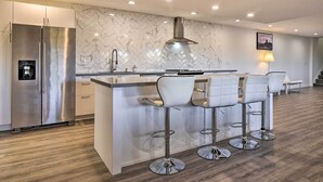 Een moderne keuken met een roestvrijstalen koelkast, een marmeren spatwand en een bar met witte krukken.