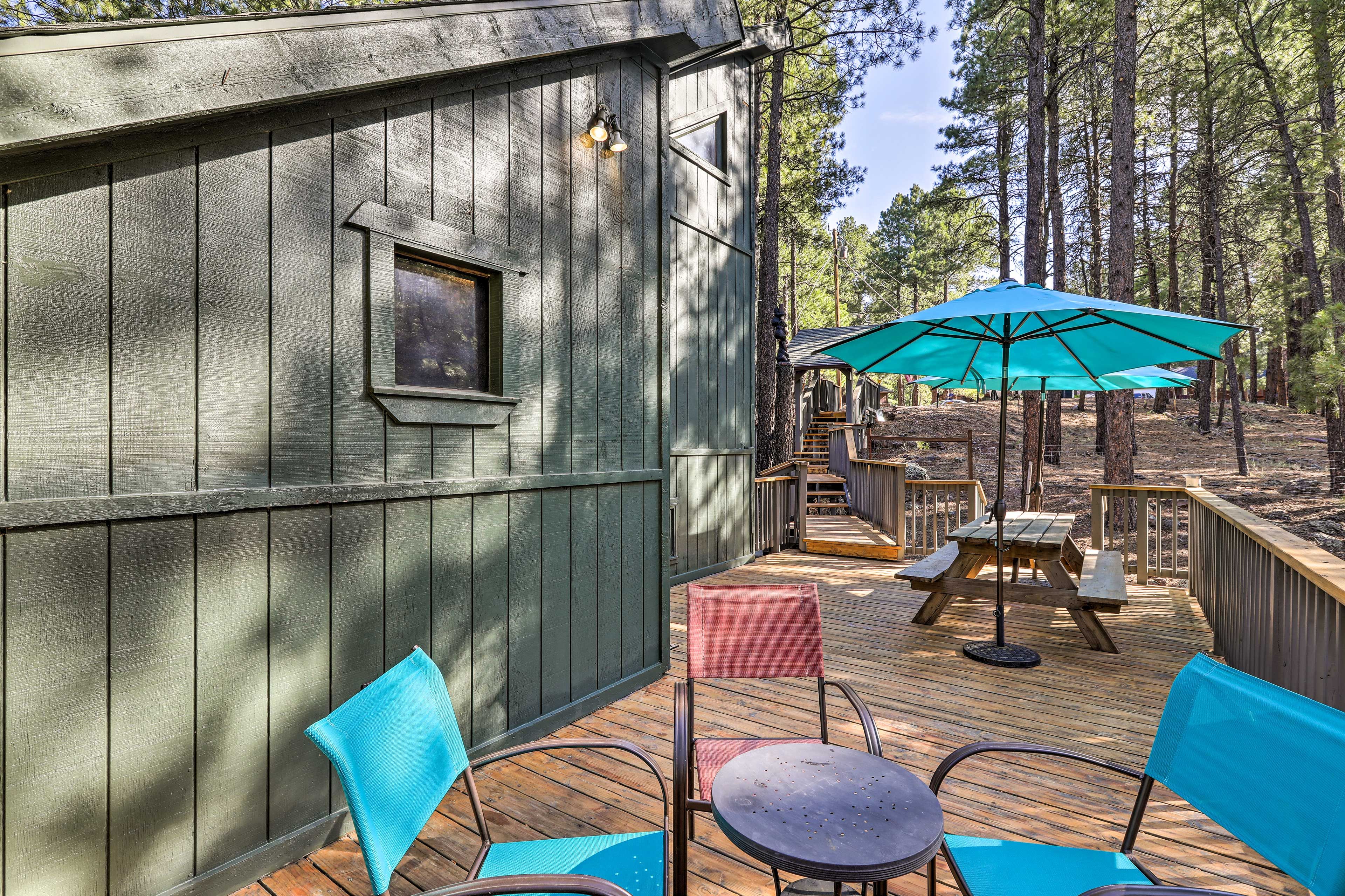 A wooden deck with outdoor seating, a small building with a window, and a forested background.