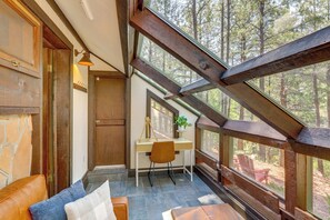 Una habitación con techo inclinado, un escritorio de madera, una silla y vistas al bosque a través de amplios ventanales.