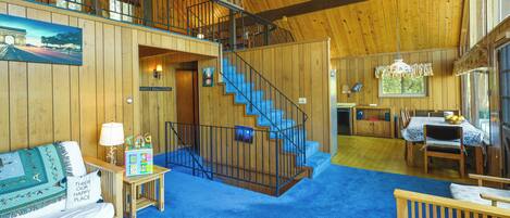 A spacious interior with a wooden staircase, a dining area, and a living room with a blue carpet.