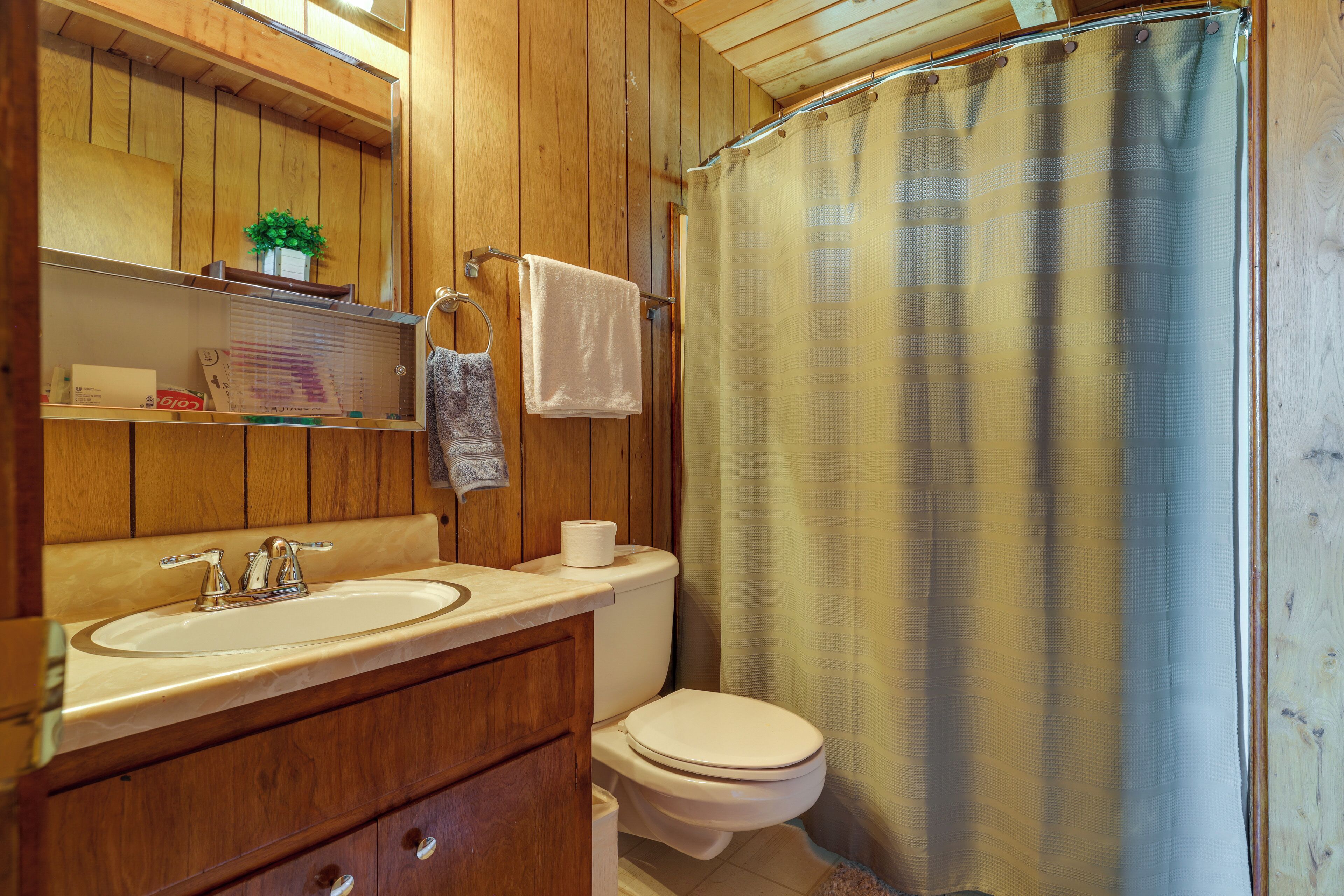 A wooden-paneled bathroom with a sink, toilet, and shower curtain.