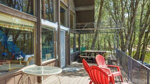 A covered outdoor area with a glass table and red chairs, surrounded by wooden deck and metal railings. - Hike, Bike & Golf: Peaceful Cabin in Twain Harte! (Twain Harte)