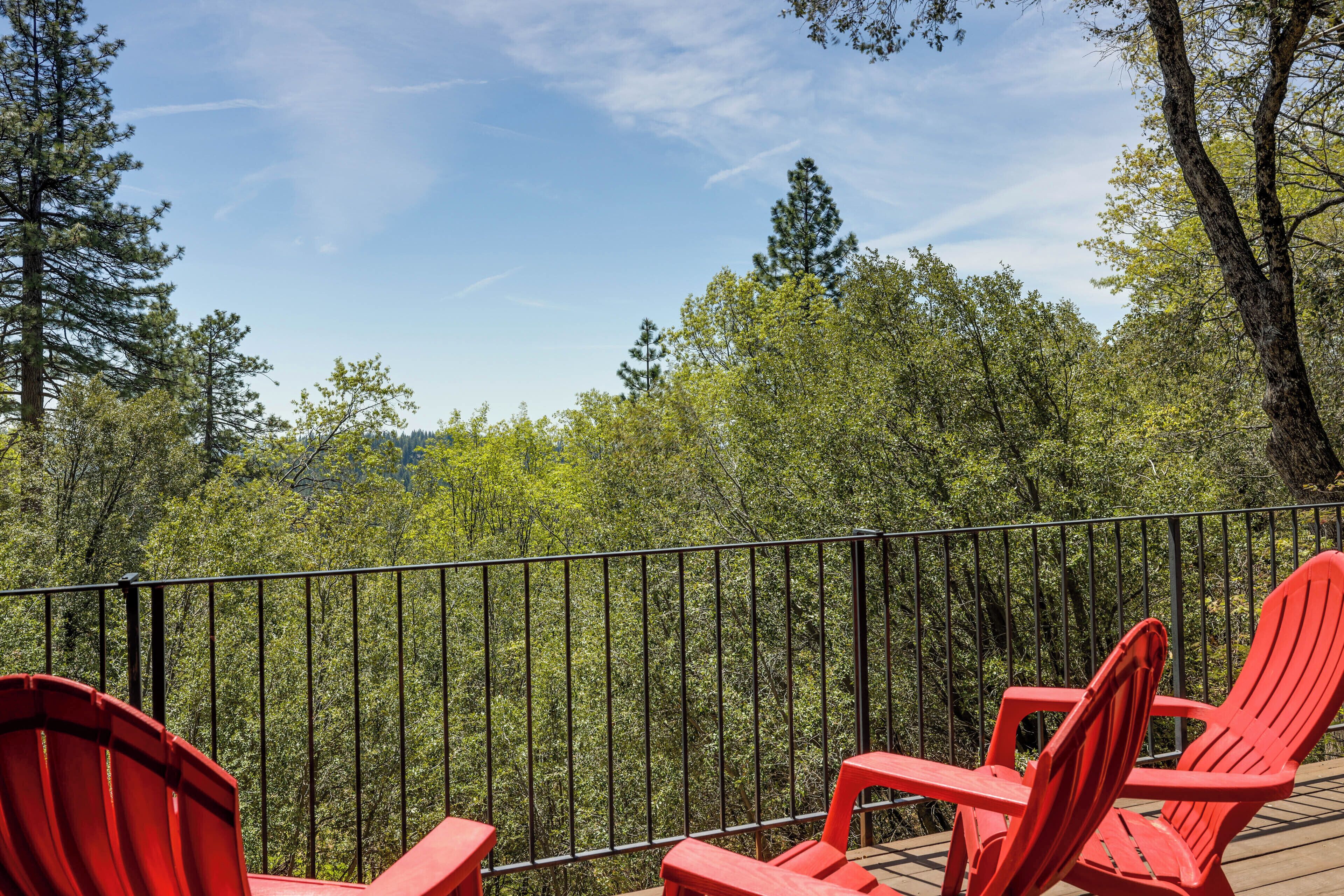 Μια ξύλινη βεράντα με κόκκινες πολυθρόνες Adirondack, από την οποία φαίνεται μια δασώδης περιοχή.