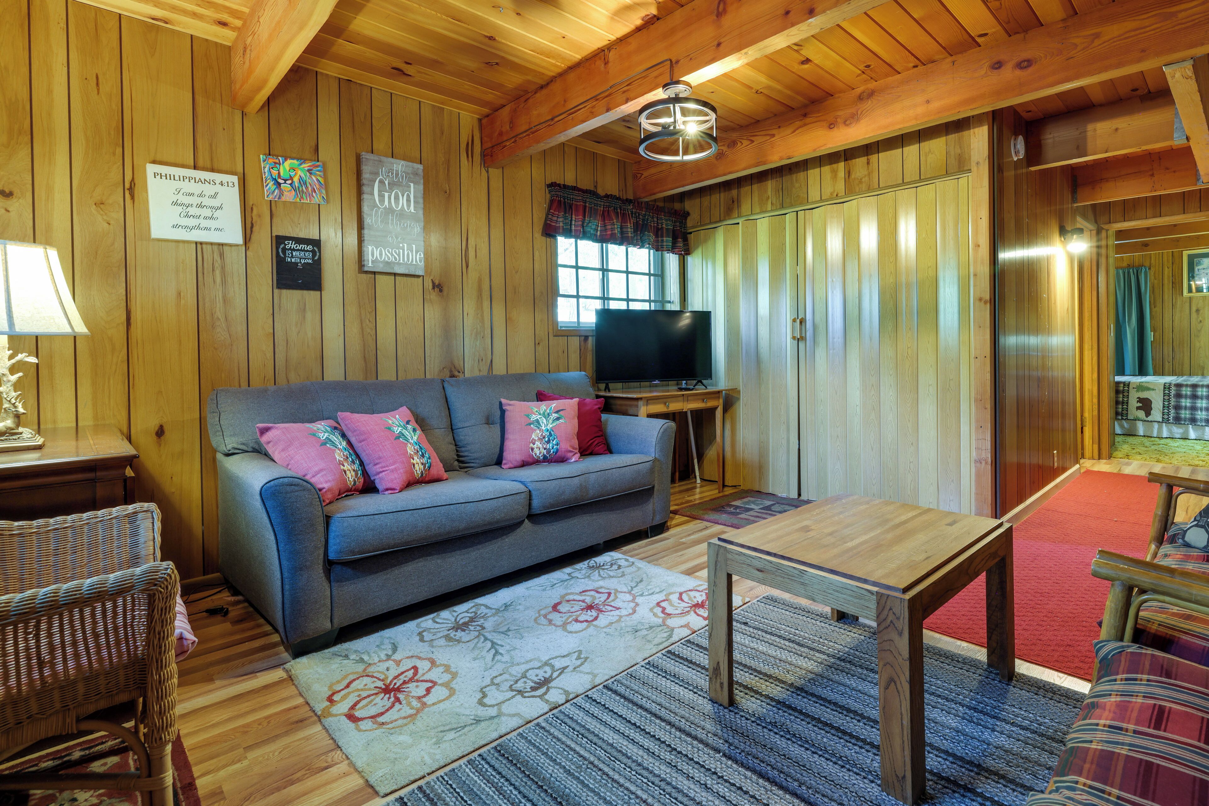 Interior acogedor de una cabaña con techo de madera, un sofá con almohadones coloridos, un televisor y una mesa de comedor.