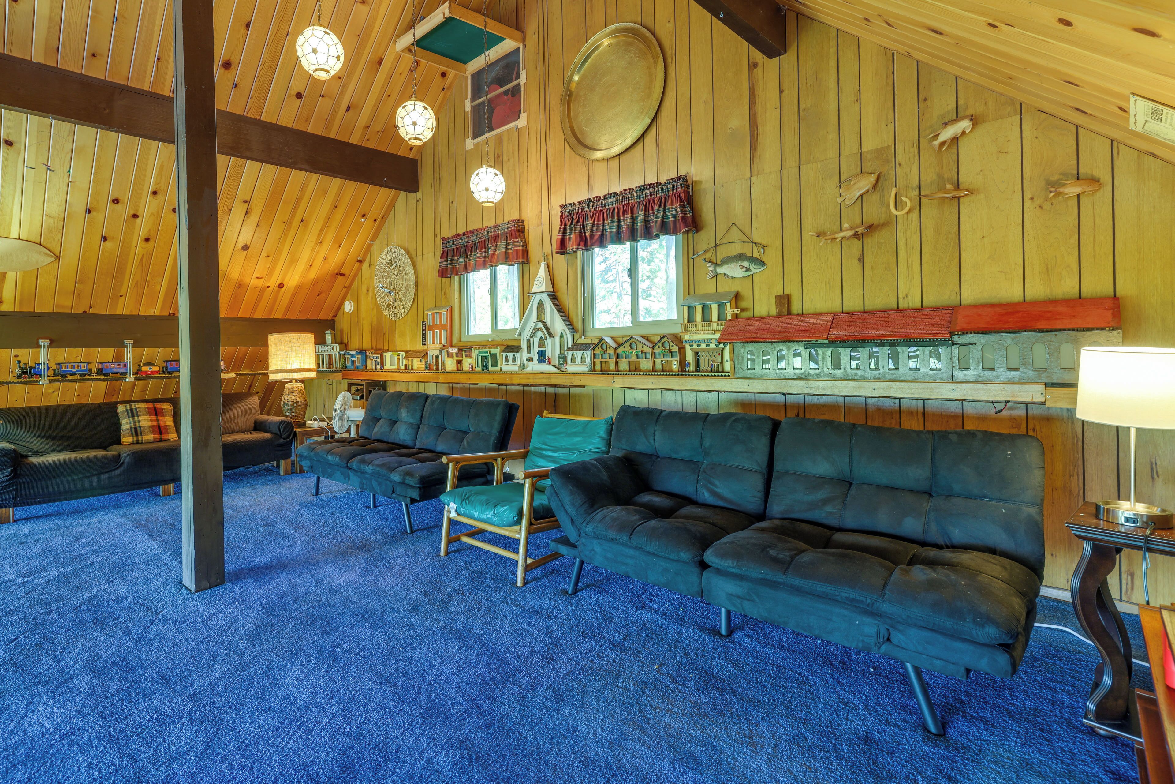 A spacious room with a high ceiling, wooden walls, and a blue carpet. There are several sofas and chairs arranged for seating.