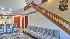 A spacious living area with a sofa, a dining table with chairs, a kitchen in the background, and a staircase. - Resort Condo w/ Lake + Pool ~ 5 Mi to Flume Gorge! (North Woodstock)