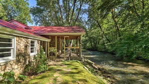 Ein Haus aus Stein mit rotem Dach, einer Veranda und einem Fluss im Hintergrund.