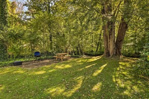 A picnic area with a table and chairs, surrounded by trees and greenery. - Waynesville Creekside Cottage: Outdoor Relaxation! (Waynesville)