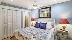 Ein Schlafzimmer mit einem Bett, zwei Nachttischlampen, einem Deckenventilator, einem Spiegel und einem Kleiderschrank.