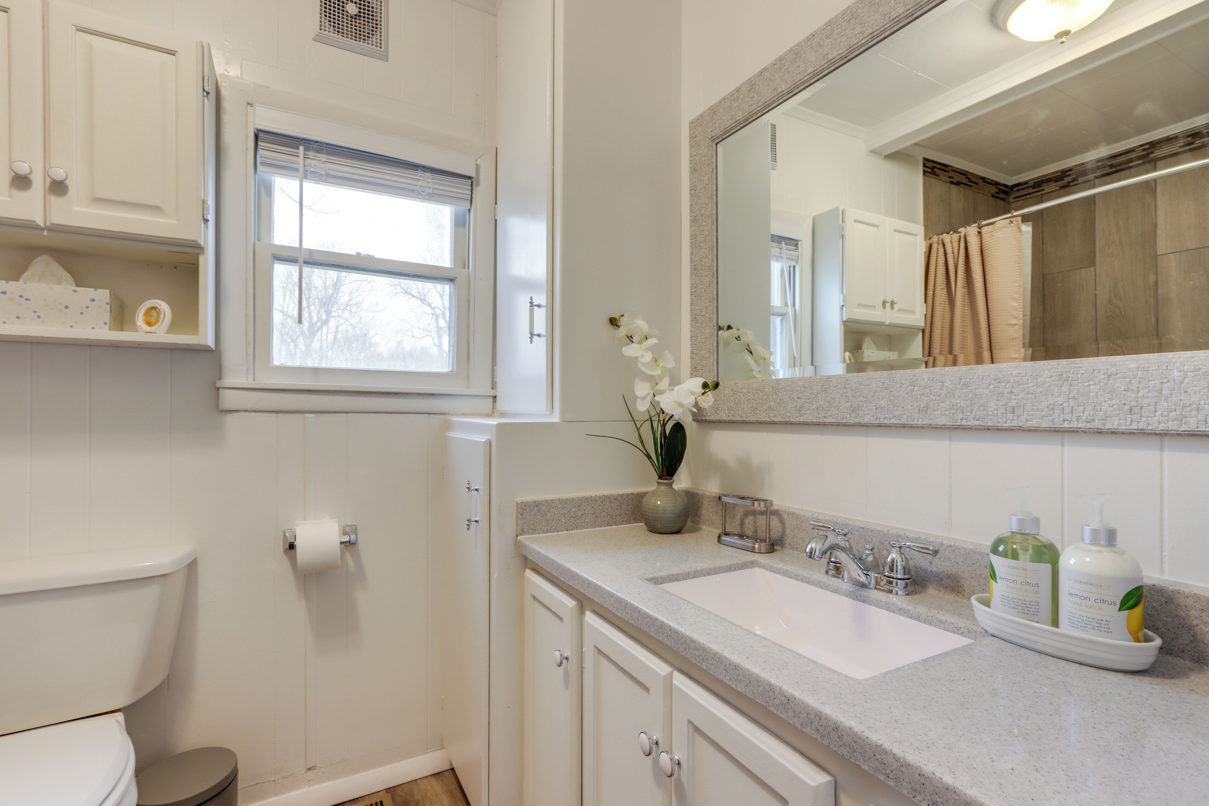 A bathroom with a toilet, sink, mirror, and window.