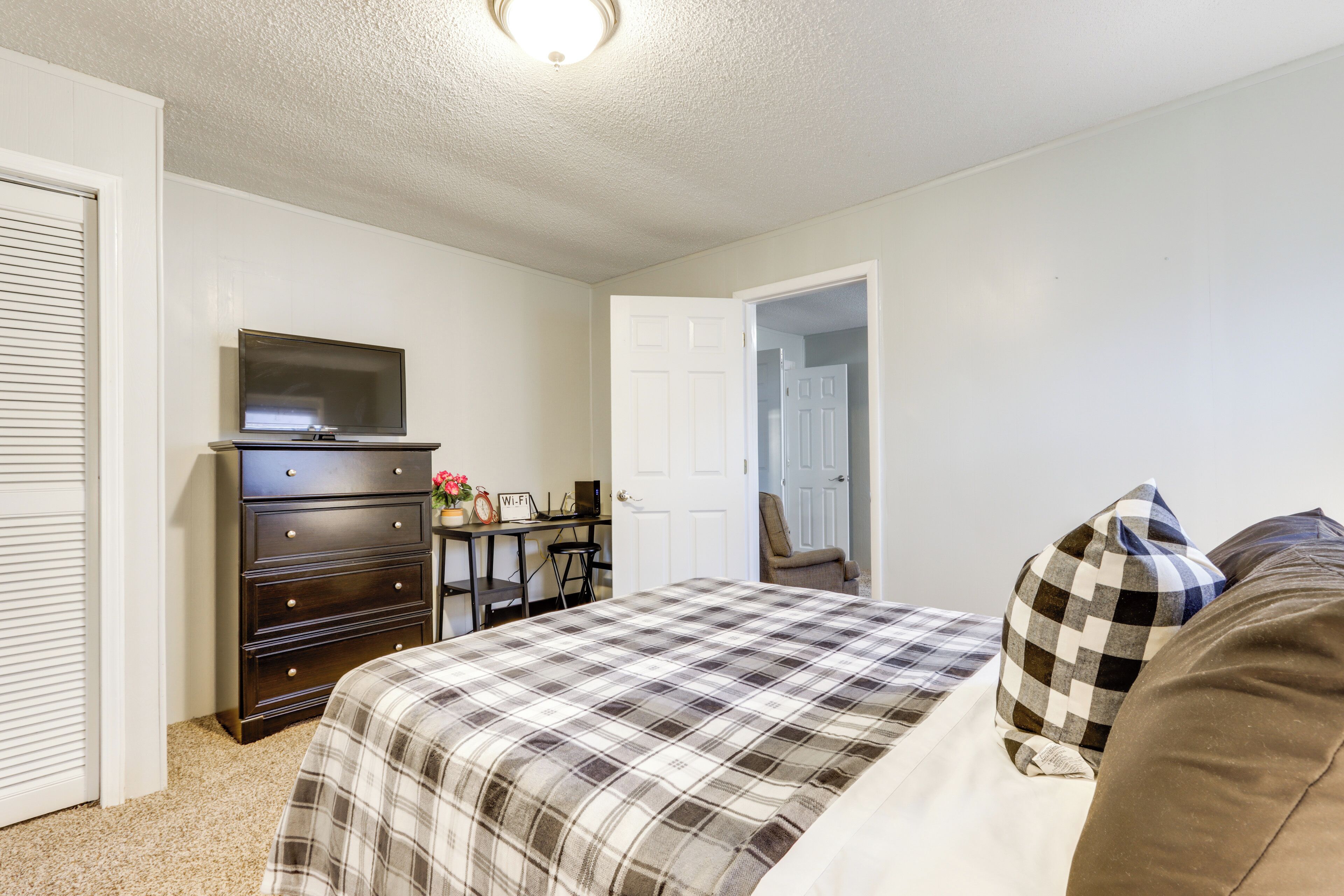 A bedroom with a bed, a dresser, a TV, and a desk with a chair.