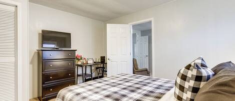 A bedroom with a bed, a dresser, a TV, and a desk with a chair.